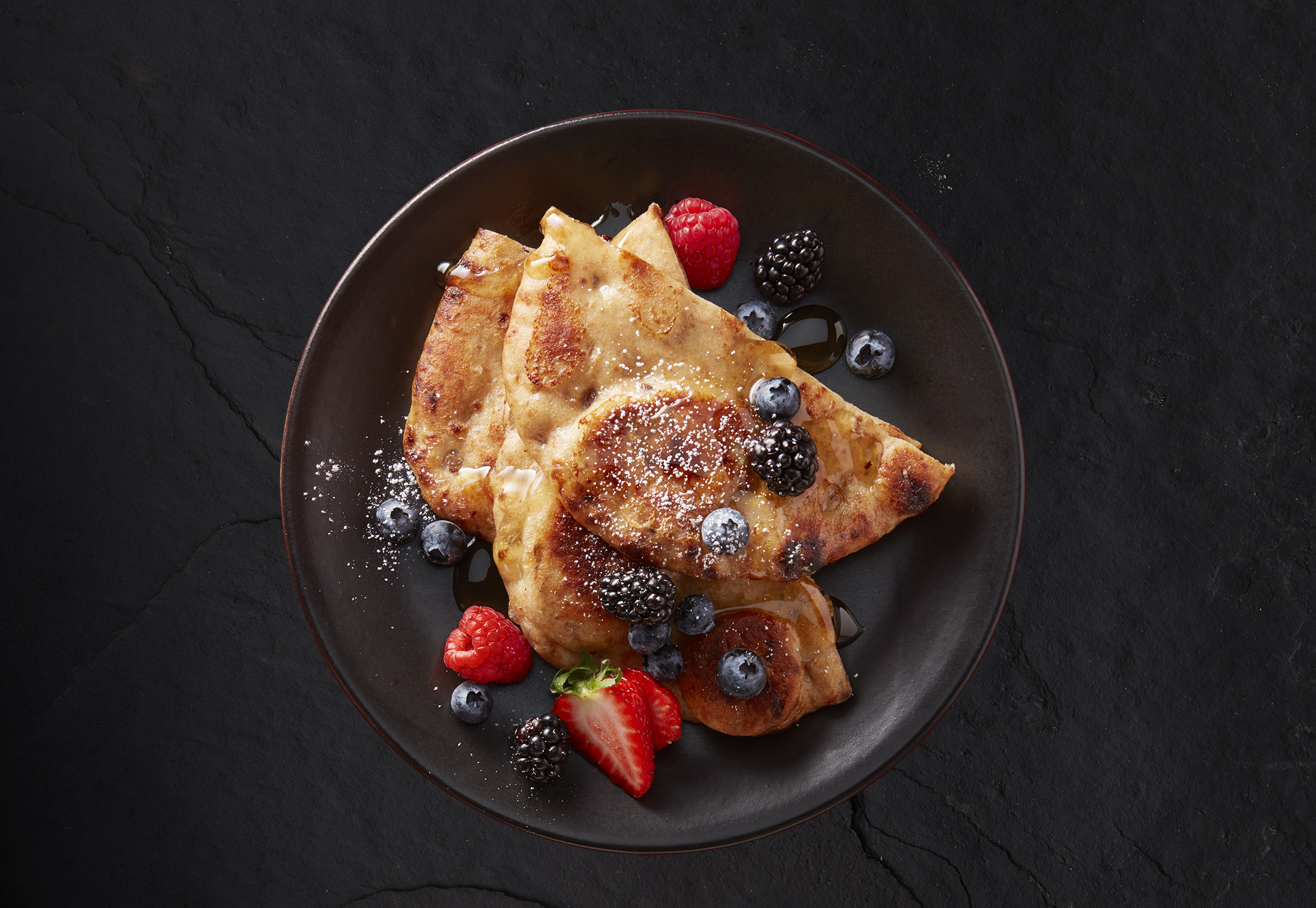 Naan pancakes topped with maple syrup, fresh strawberries, raspberries, blueberries, blackberries and icing sugar.