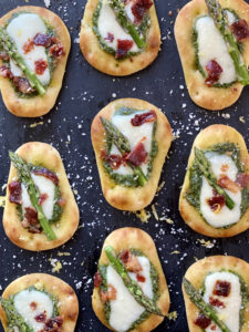 Stonefire® Naan Dippers® topped with vibrant green homemade pesto, crispy bacon, and tender asparagus for an elegant snack option."