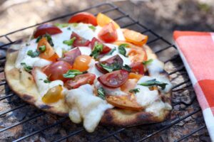 Sizzling naan pizza cooking on a campfire, surrounded by dancing flames.
